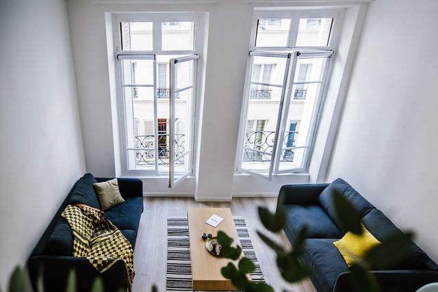 Dans le salon de ce logement parisien, les assises sont apposées contre les murs latéraux, laissant la circulation libre devant les deux grandes fenêtres. Réalisation Lara Grand Studio. 