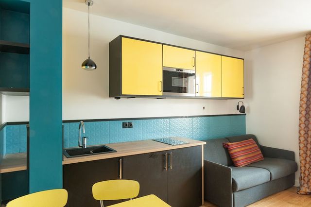 Dans ce studio, la pièce à vivre est très réduite. Il faut donc optimiser au maximum l'espace sans l'encombrer. Les touches de jaune et de bleu canard font office de fil conducteur dans la pièce. Réalisation maéma Architectes.