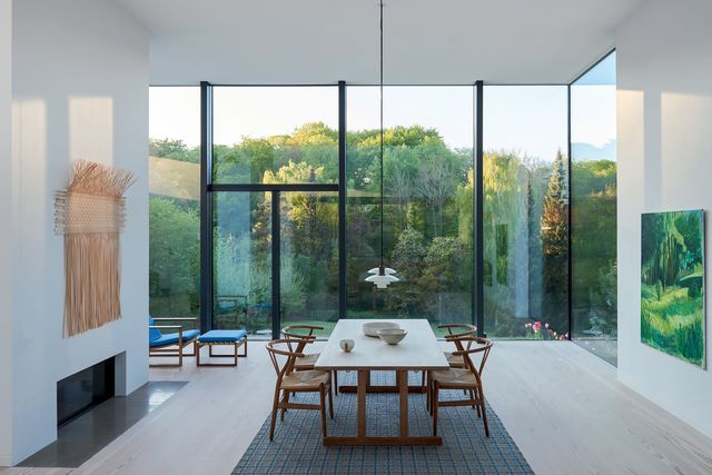 Perchée sur le jardin en pente, la maison cadre la luxuriance des arbres et espèces rares, avec la forêt en toile de fond. Avec ses structures minimalistes, ce mur de verre et autres ouvertures sur le paysage donnent l'impression d'un tableau, dans un jeu de miroir avec celui du Danois Iver Villefranche qui pourrait être une fenêtre sur l'extérieur. Longitudinal, le tapis de Patricia Urquiola pour Gianda Blasco dirige le regard, tandis qu'une décoration épurée complète la perspective sous quatre mètres de plafond : table et fauteuil bleu de Børge Mogensen, chaises "Y" d'Hans Wegner, suspensions de Poul Henningsen, petit bol japonais, coupe de KH Würtz.